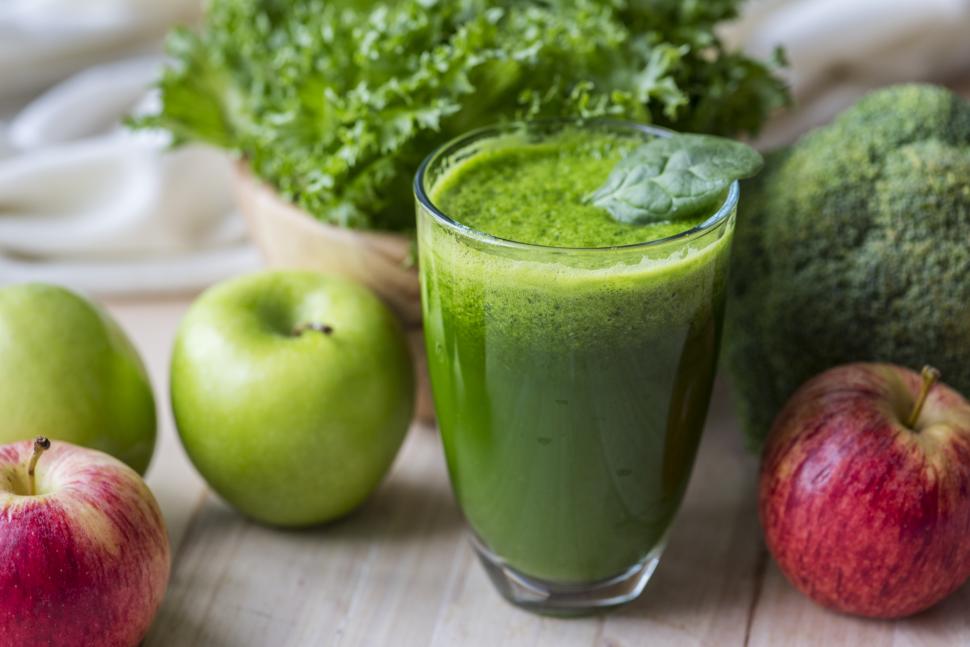 Green juice surrounded by apples and other produce
