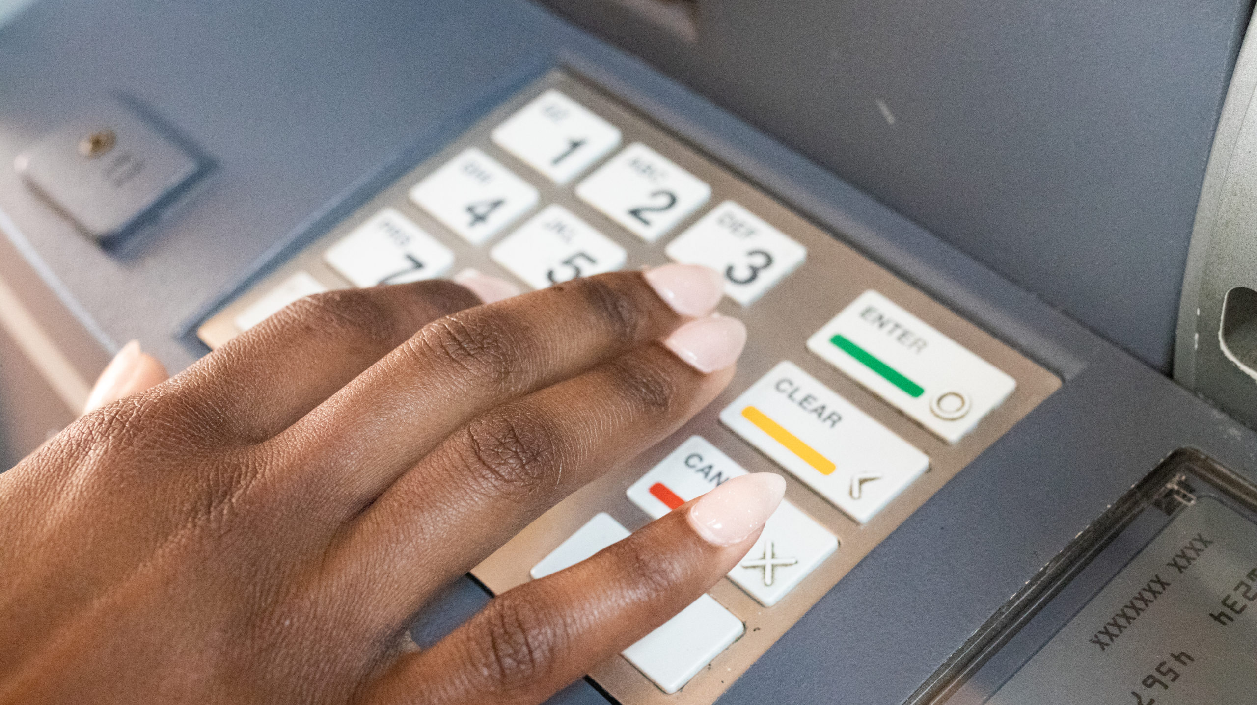 Close up of woman's hand pressing keys on keypad of automated teller machine (ATM)