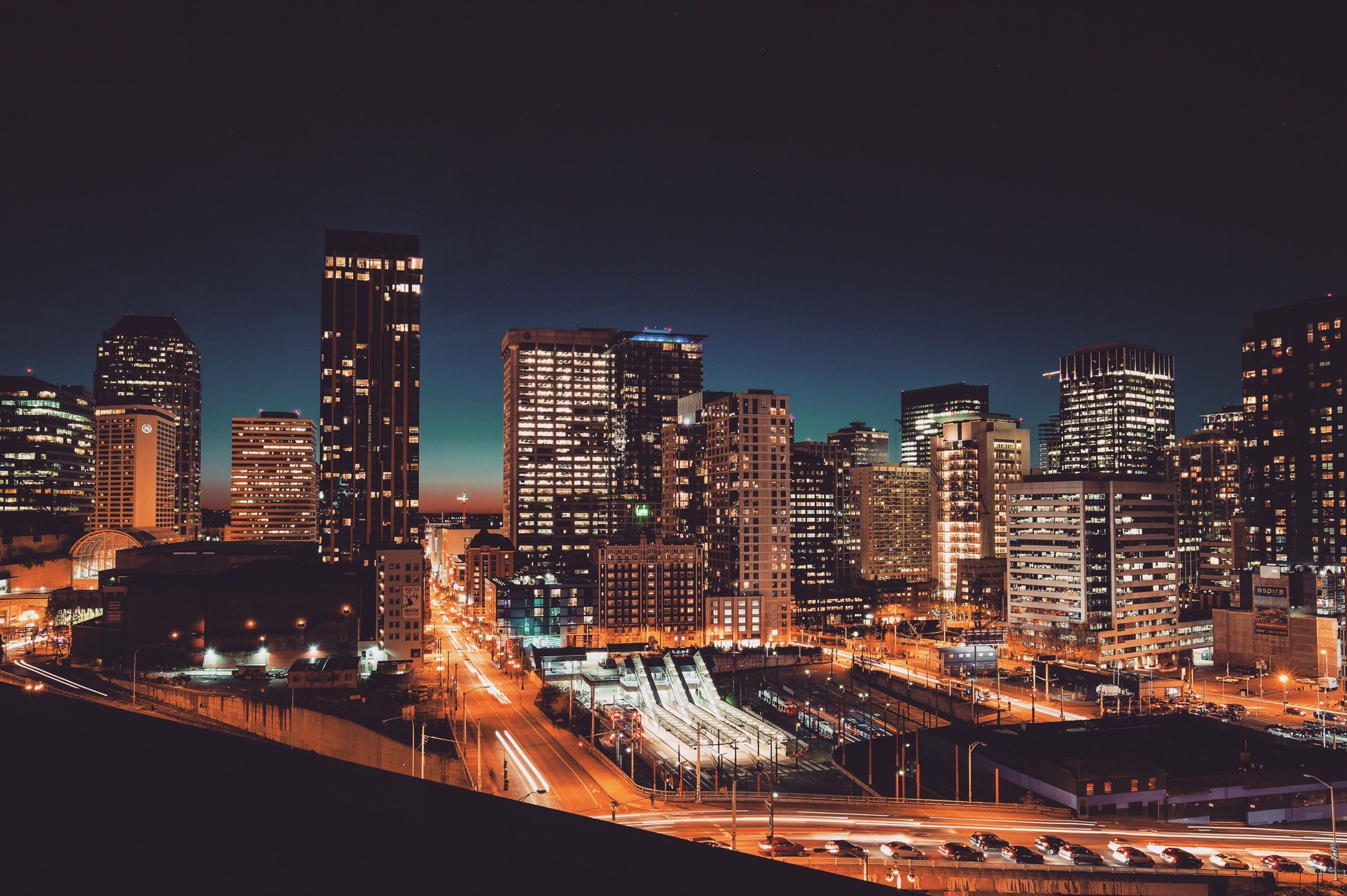 A city skyline at night with a busy freeway and blurred headlights.