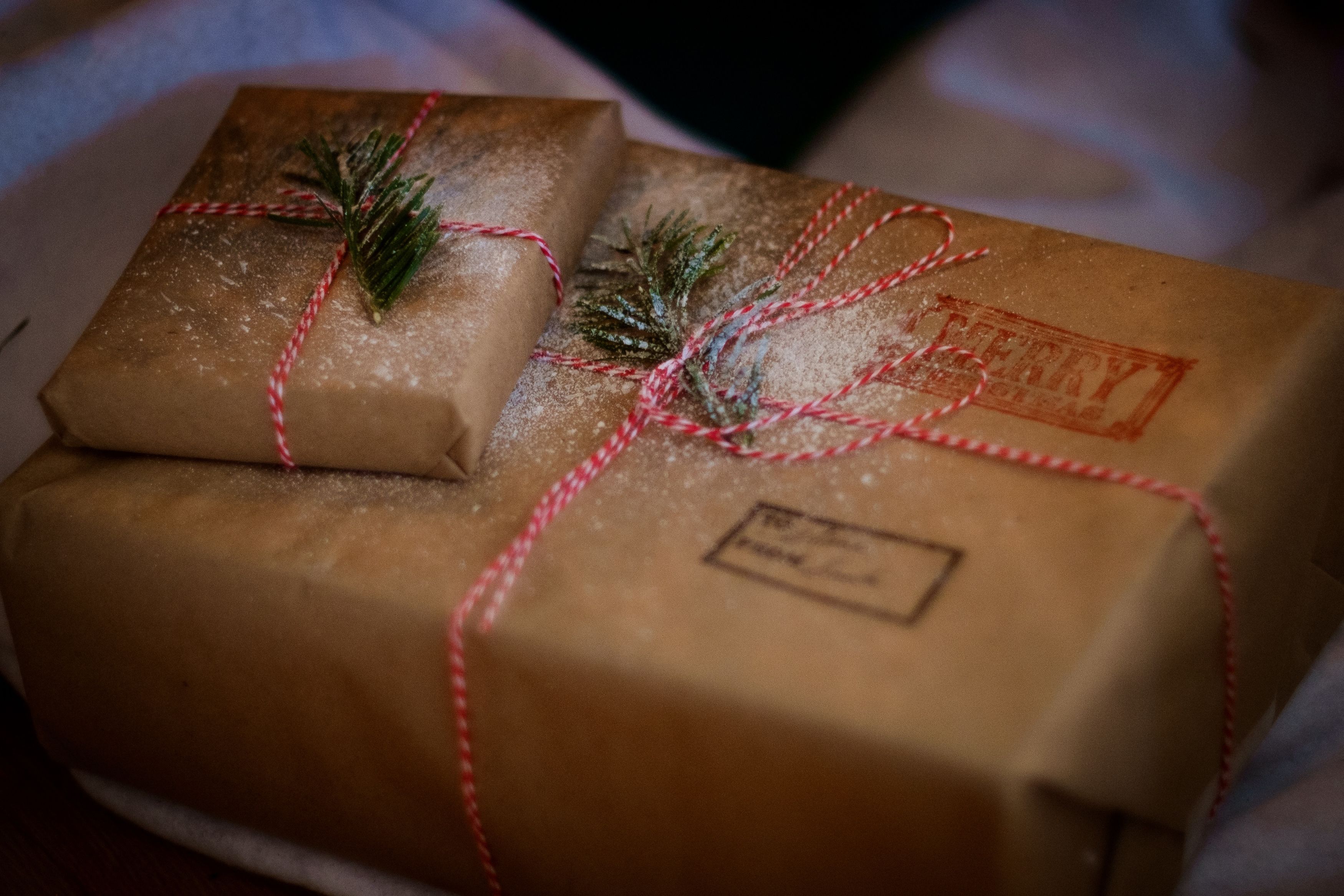 Gifts wrapped in brown paper and twine, with sprigs of evergreen and a soft dusting of snow on top of them.