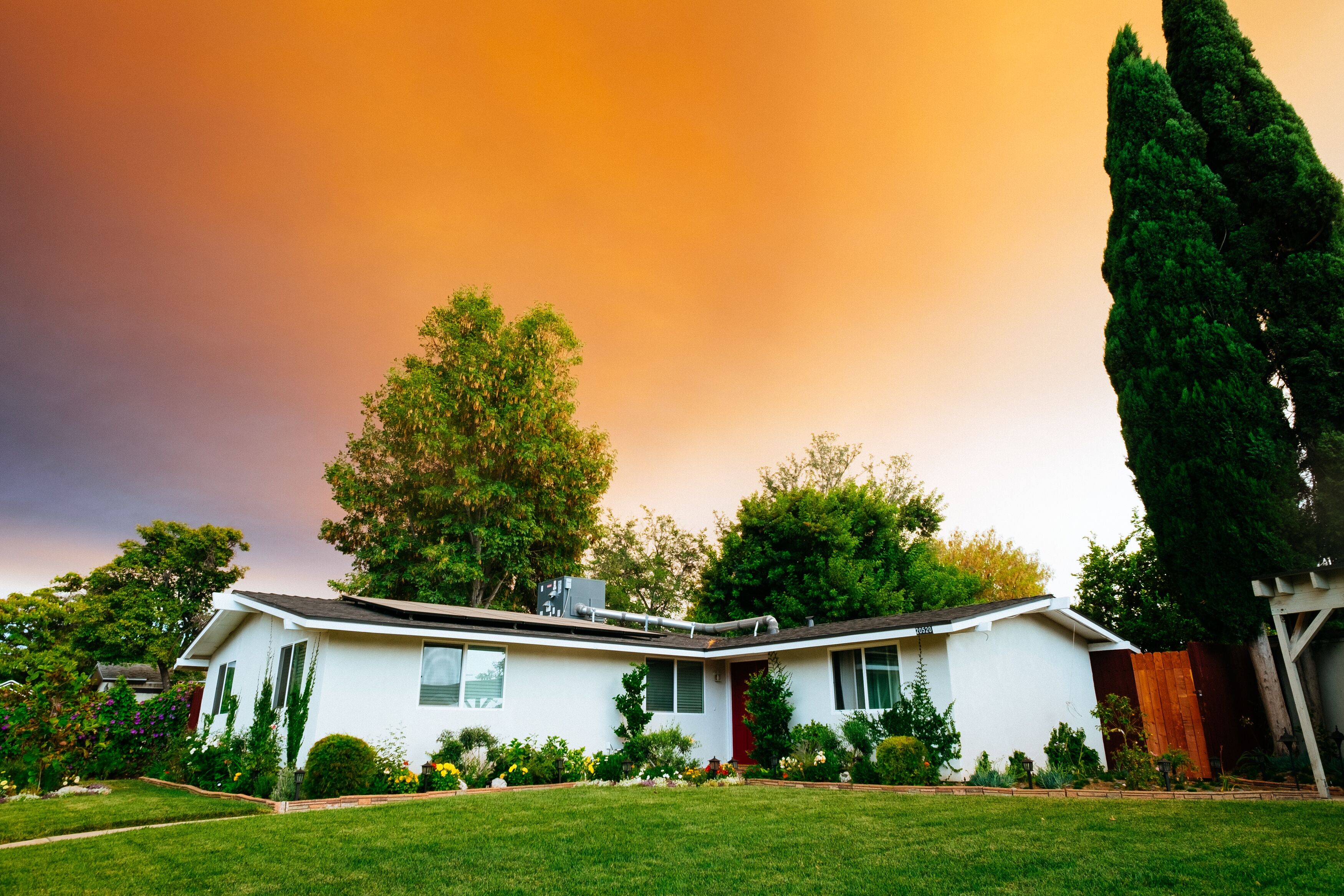 A single-story house with a well-manicured lawn under a sky with a dramatic orange sunset