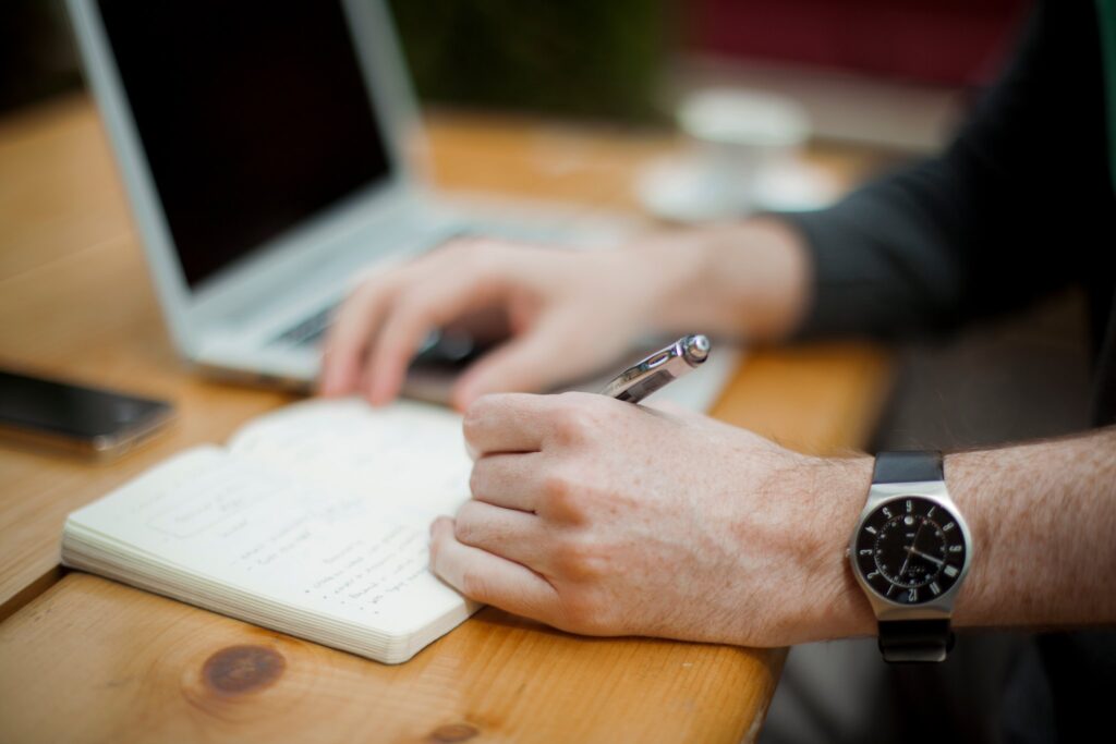 Hands of someone writing in a notebook and working at a computer.