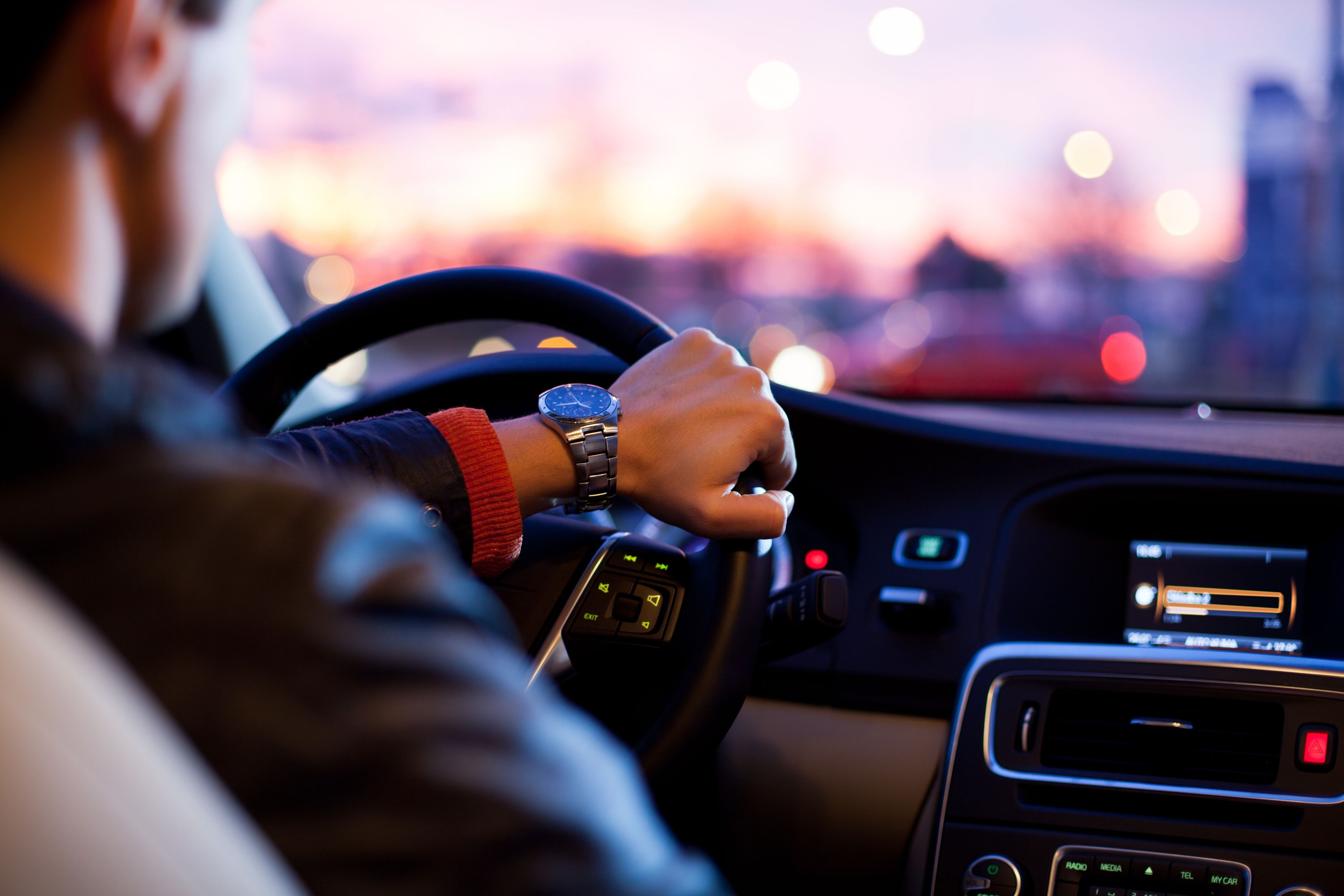 Man driving a car at sunset with pink and purple skies.