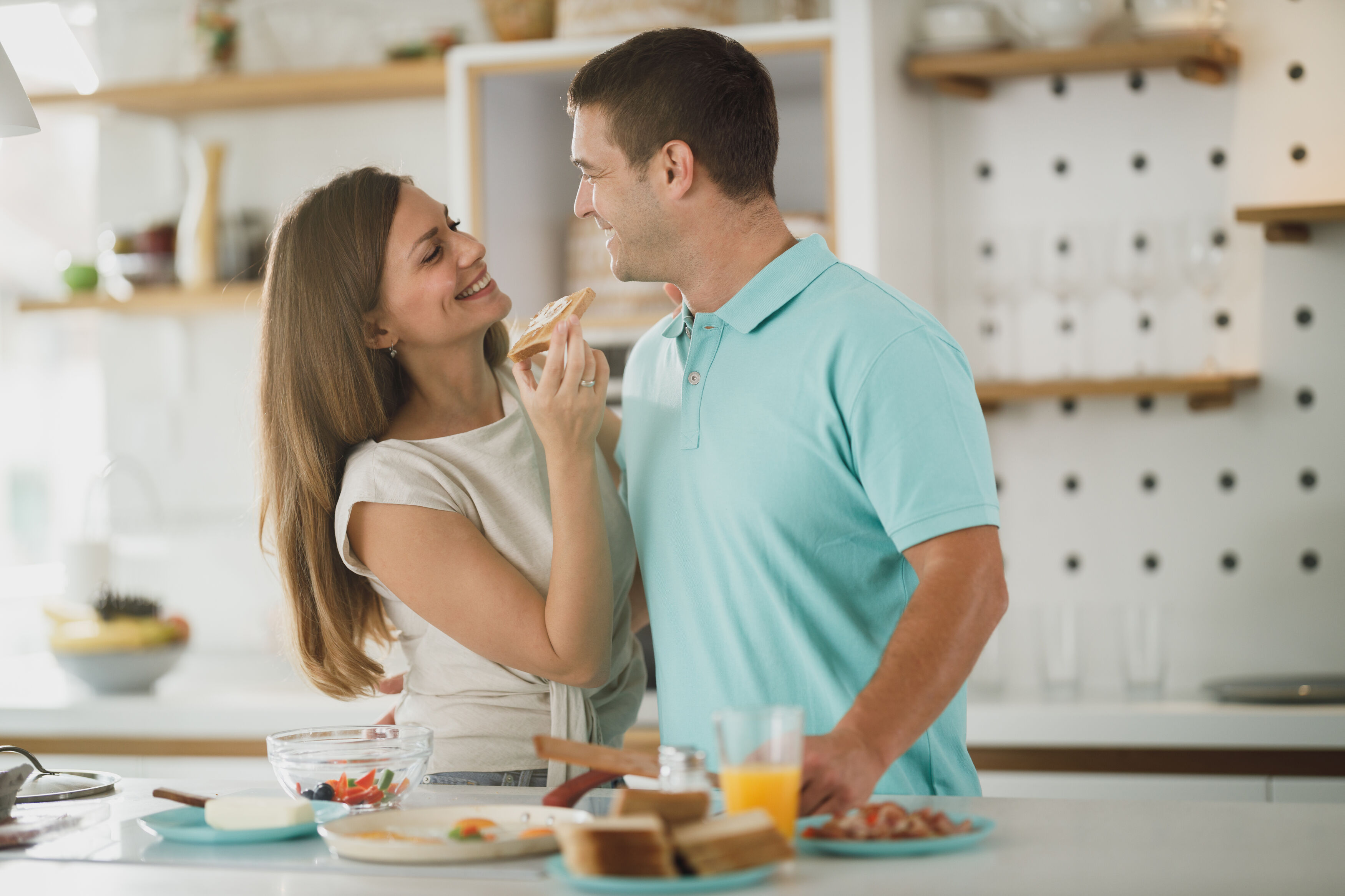 A young couple shares a joyful moment while tasting food in a well-equipped kitchen with a modern interior