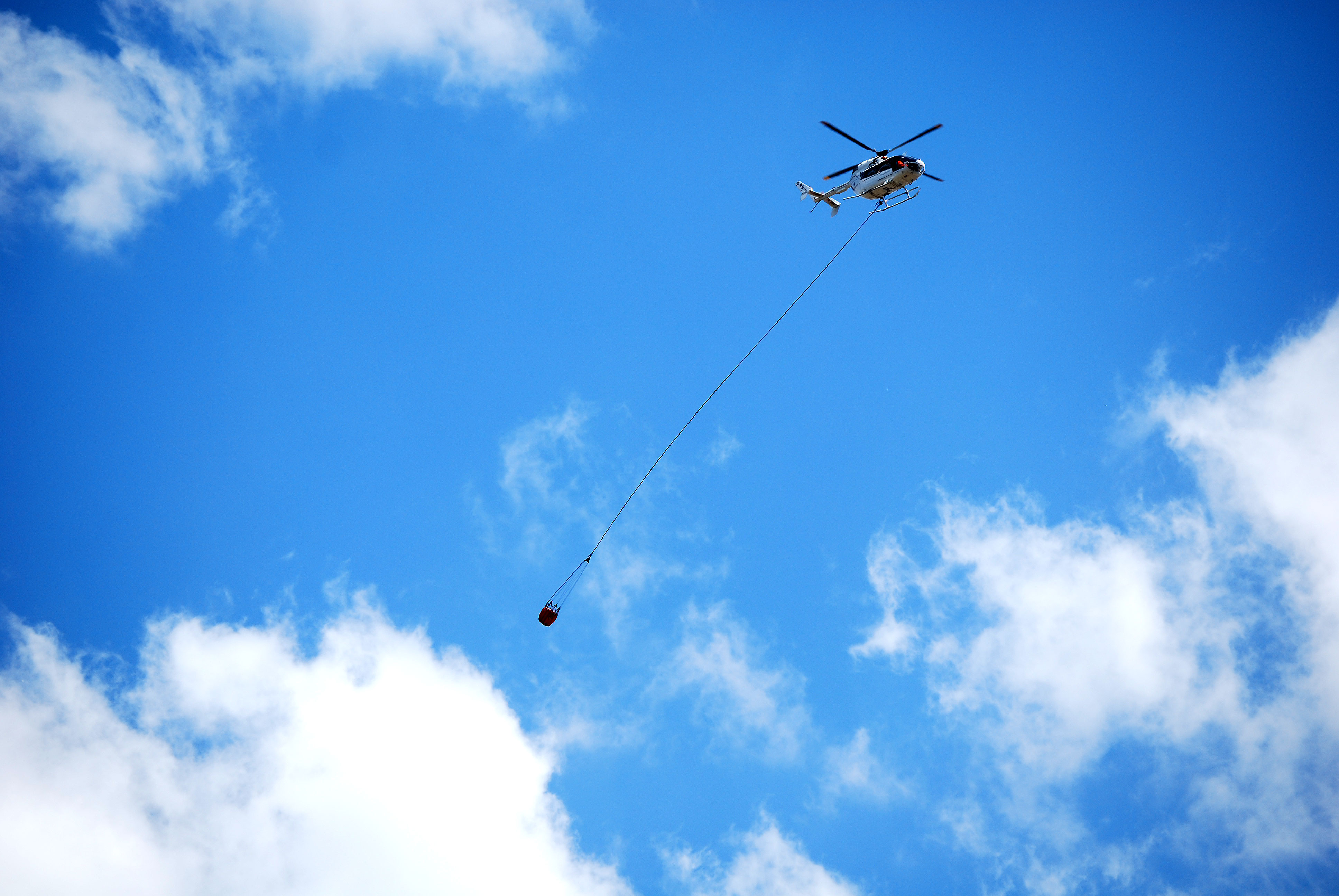 Helicopter prepares to fight fire with water bucket.