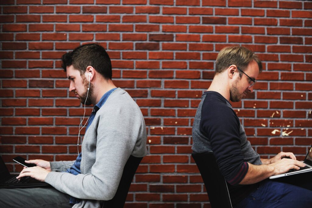 Two men working back to back in front of a brick wall.