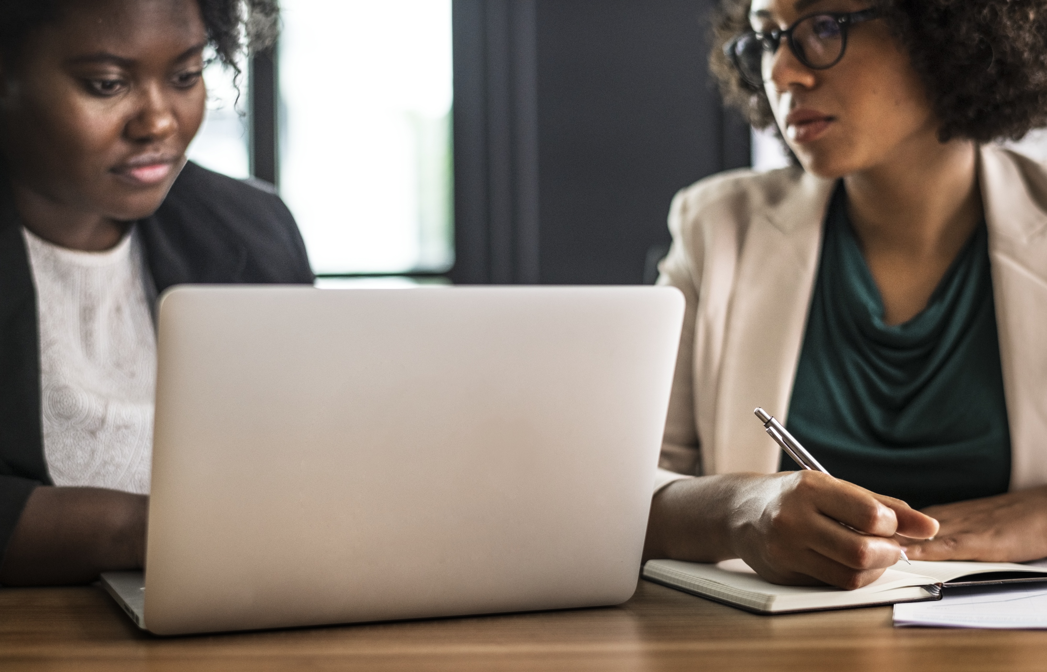 Two Black women working in the office looking at the laptop screen checking their Business Tax Account maybe.