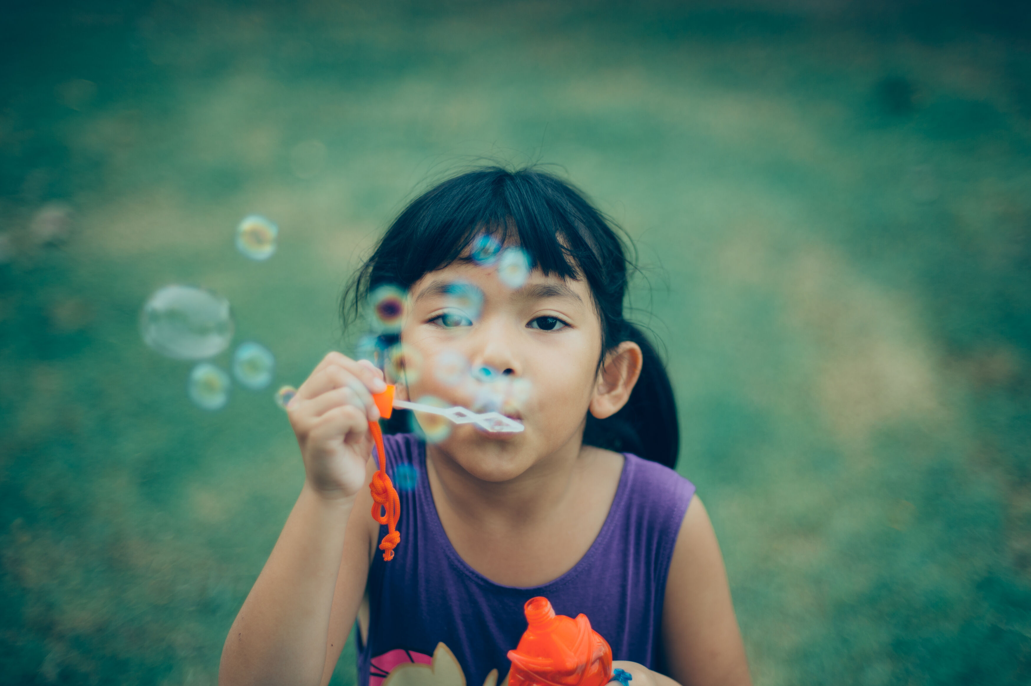 A young girl is blowing soap bubbles concentrate outdoors on a sunny day, with selective focus on her face.