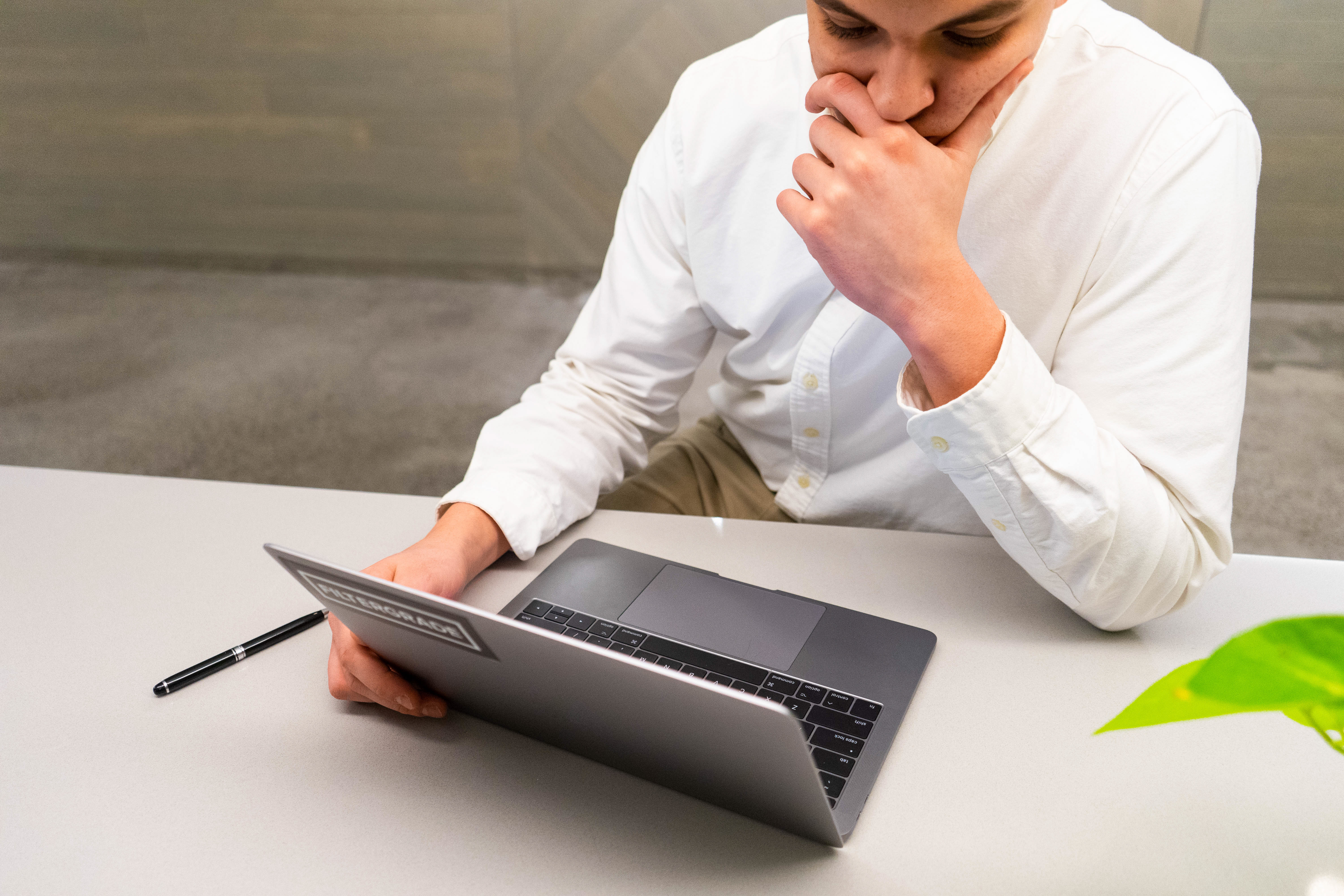 Young pensive Caucasian businessman in white shirt working with laptop at the office desk